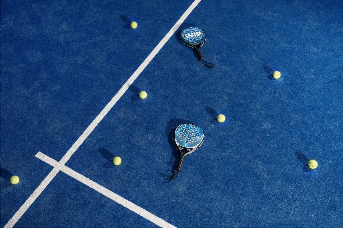Raquettes et balles de padel posées sur un court bleu, vue depuis le fond du terrain