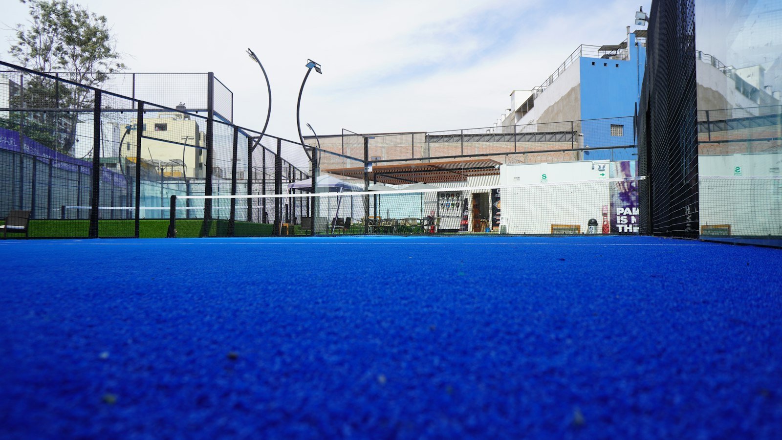 Piste de padel bleue vue depuis le fond du court, avec filet central, lignes de service et parois vitrées