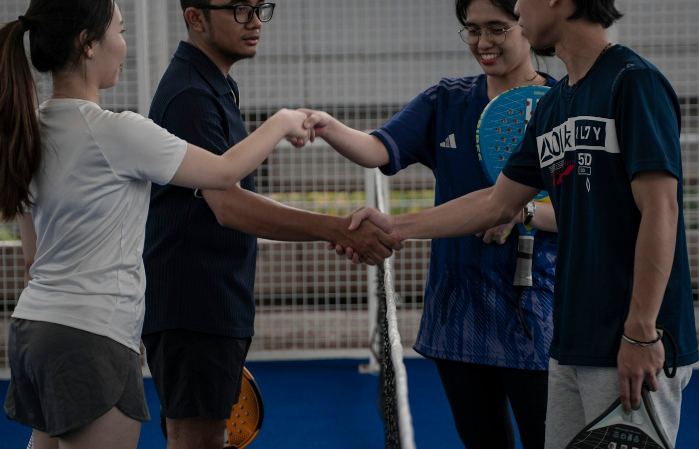 Quatre joueurs de padel se serrent la main au-dessus du filet après un match en salle