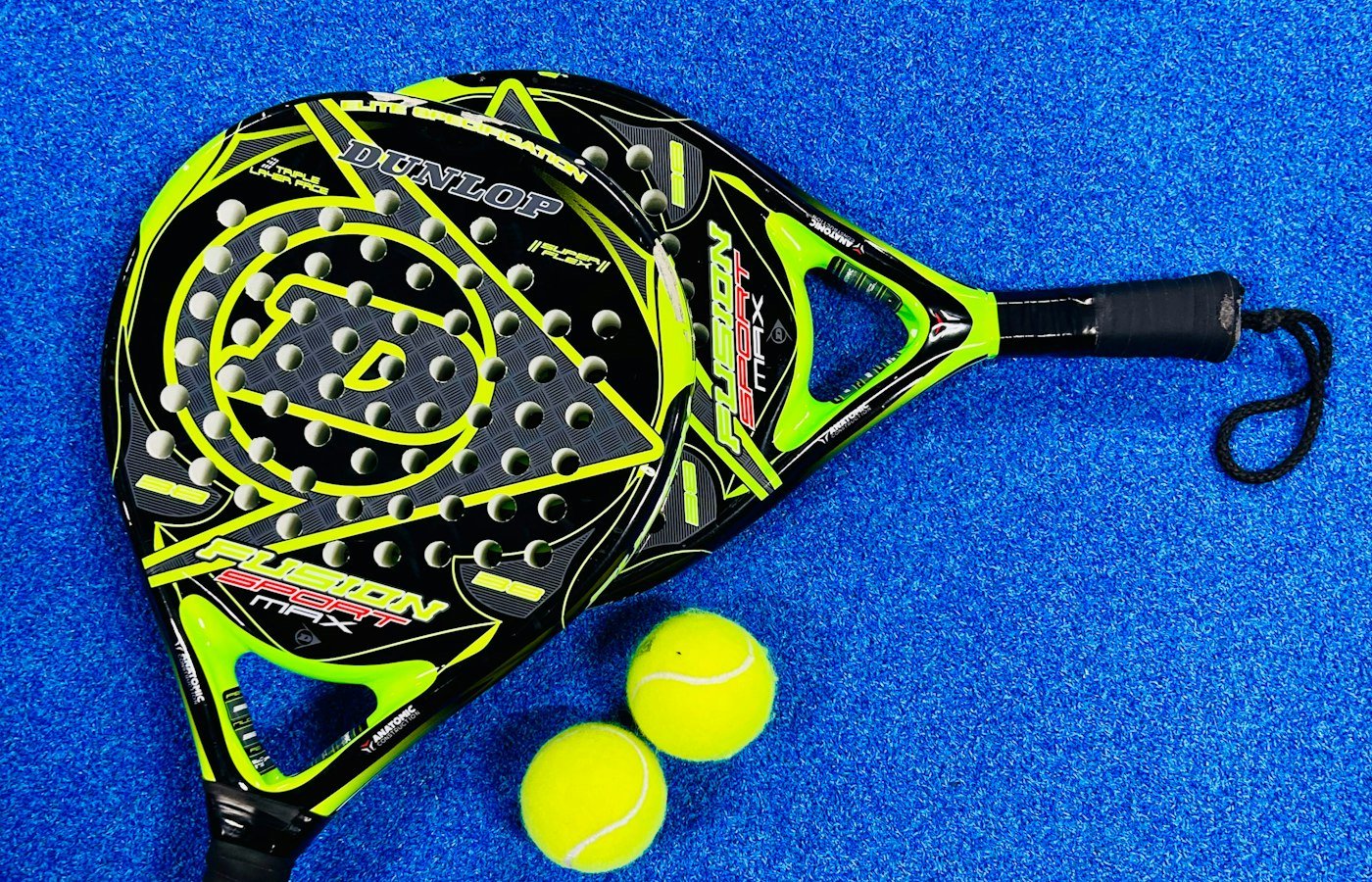 Raquette de padel noire et jaune posée avec deux balles sur un gazon synthétique bleu