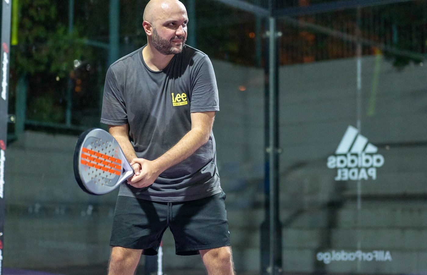 Joueur de padel en position d’attente sur un court violet, raquette tenue devant lui à deux mains