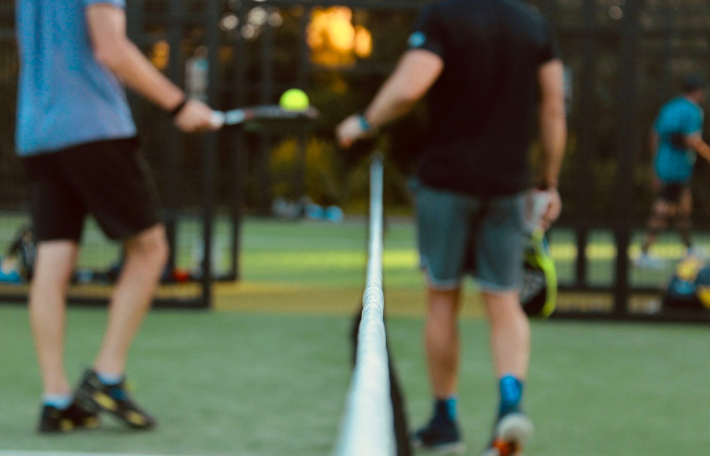 Deux joueurs de padel face à face au filet, raquettes levées, balle jaune en l’air