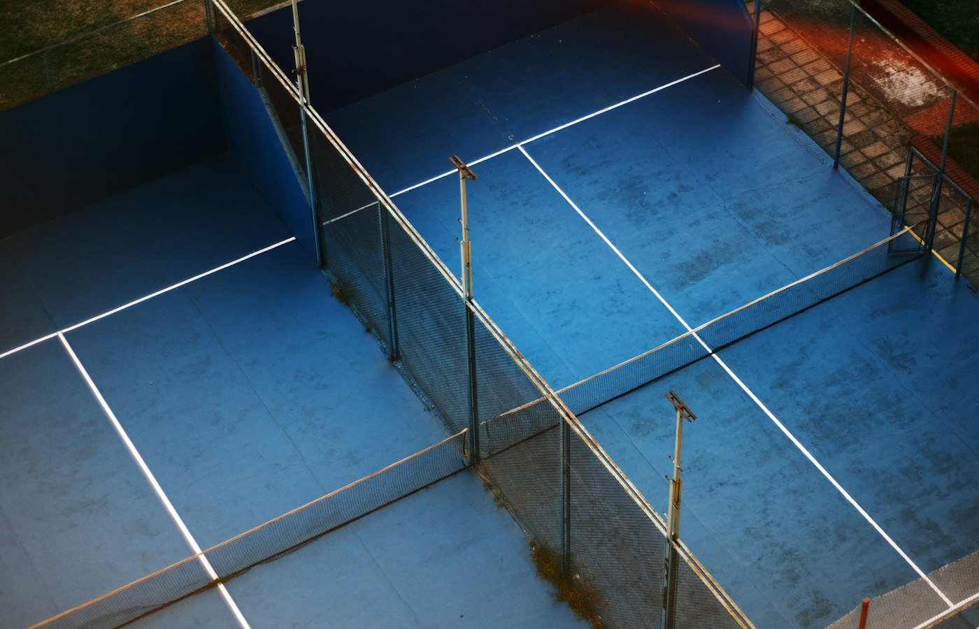 Terrains de padel bleus vus d’en haut, séparés par des vitres et un grillage