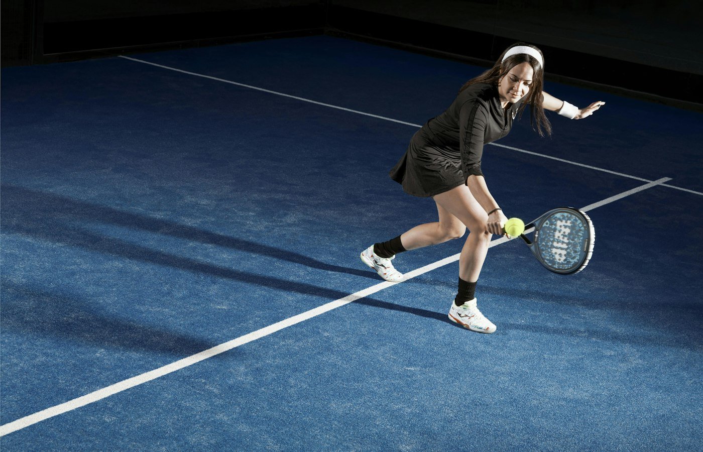 Joueuse de padel fléchie sur les jambes qui joue une balle basse près du sol, sur un court bleu