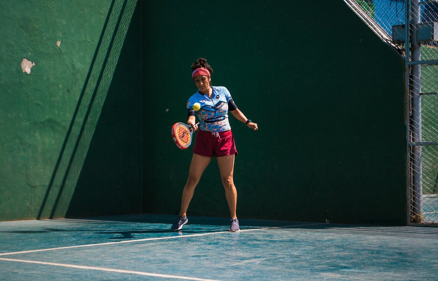 Joueuse de padel en bandeau rose qui frappe une balle devant le mur vert du fond