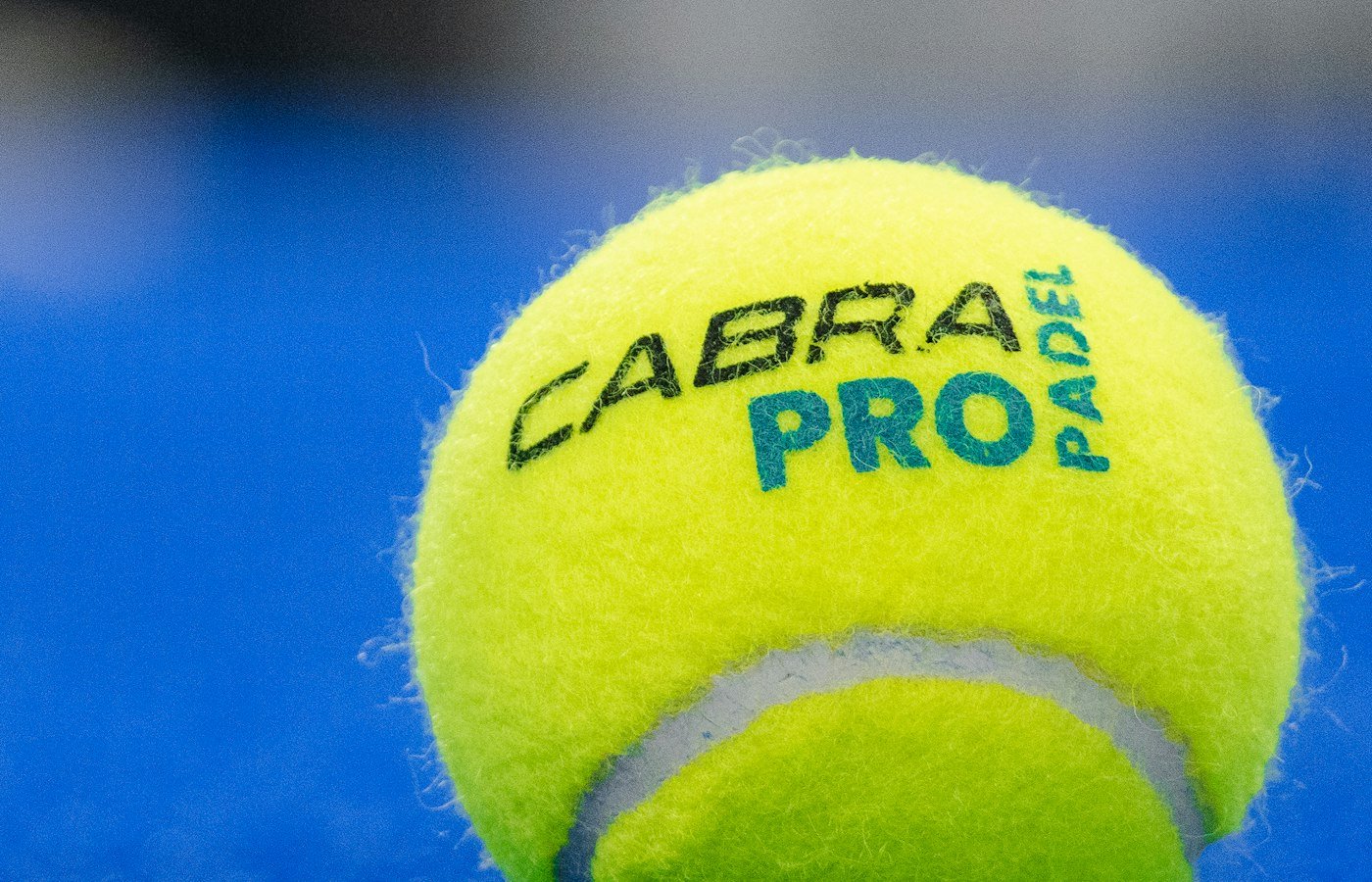 Gros plan d’une balle de padel jaune Cabra Pro posée sur un gazon synthétique bleu