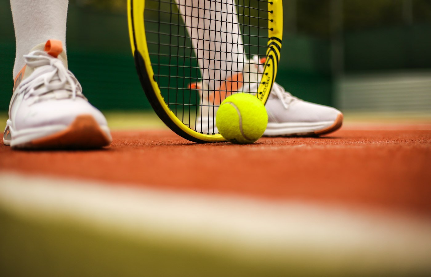 Joueur en baskets blanches avec raquette et balle sur un court en terre battue