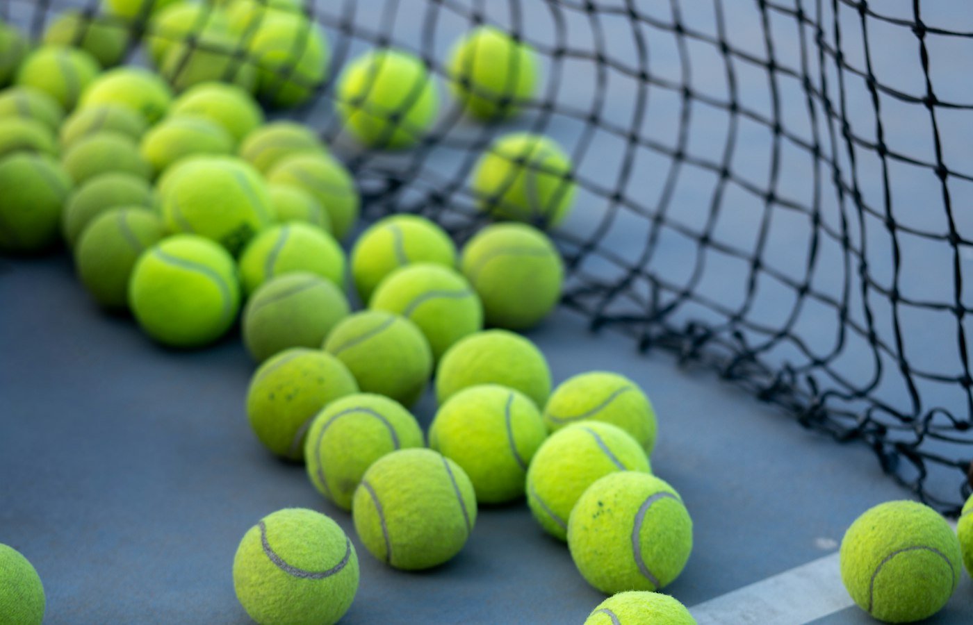 Balles jaunes au pied du filet sur un court bleu
