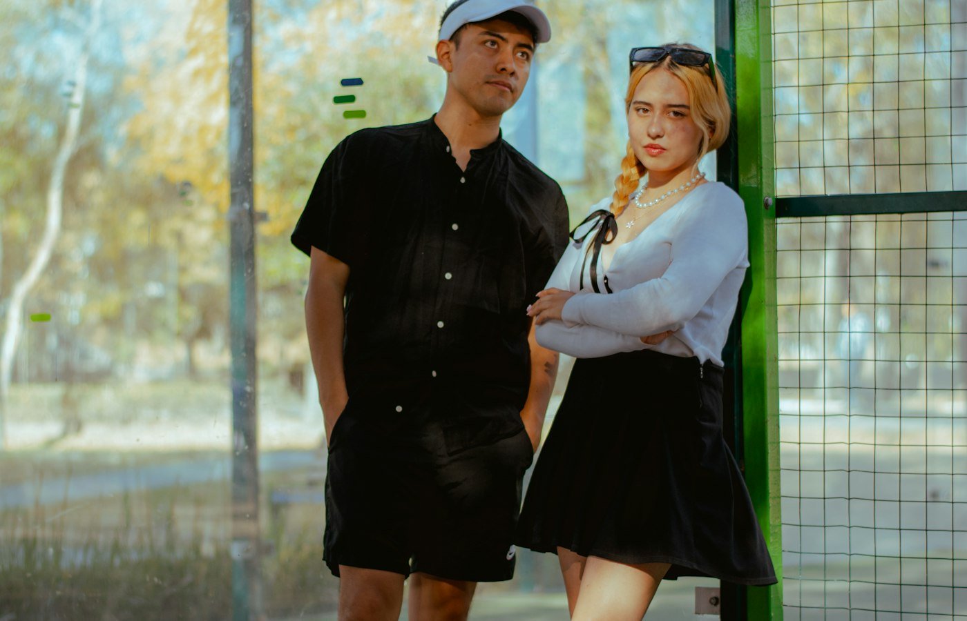 Un homme et une femme posent côte à côte devant le grillage d’un court de padel extérieur