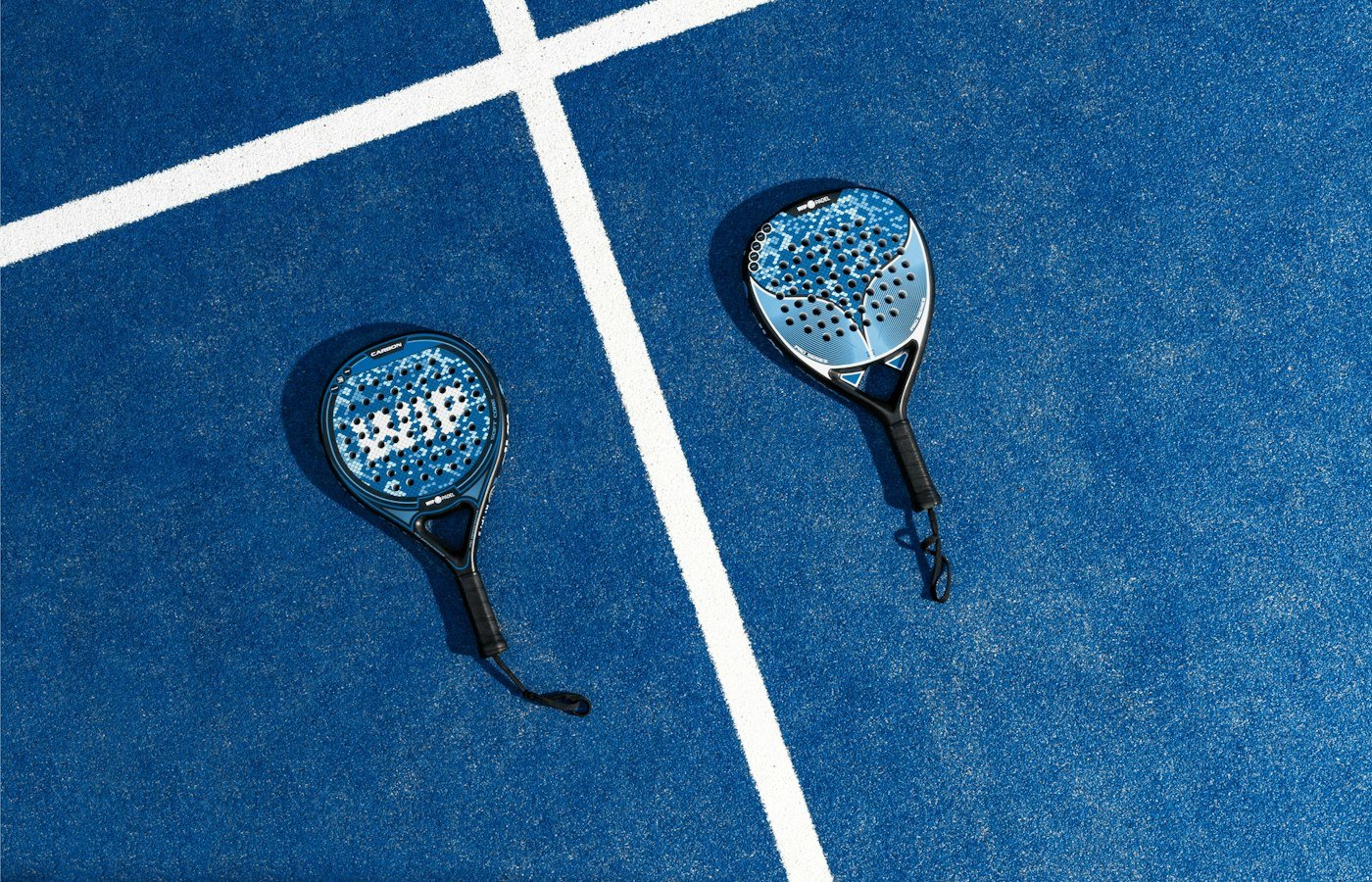 Deux raquettes de padel posées sur un court bleu, près des lignes blanches