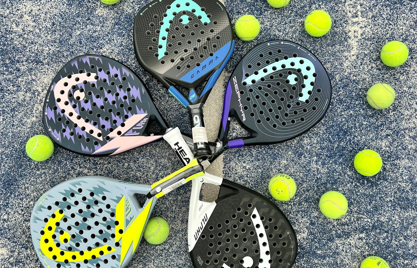 Quatre raquettes de padel disposées en cercle au milieu de balles jaunes sur un gazon synthétique bleu