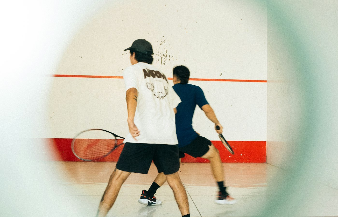 Deux joueurs de squash avec leurs raquettes sur un court en salle, mur blanc derrière eux