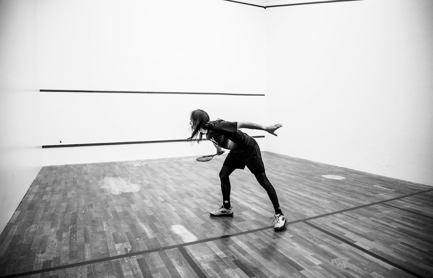 Joueuse de squash en appui sur un court en parquet, photo en noir et blanc