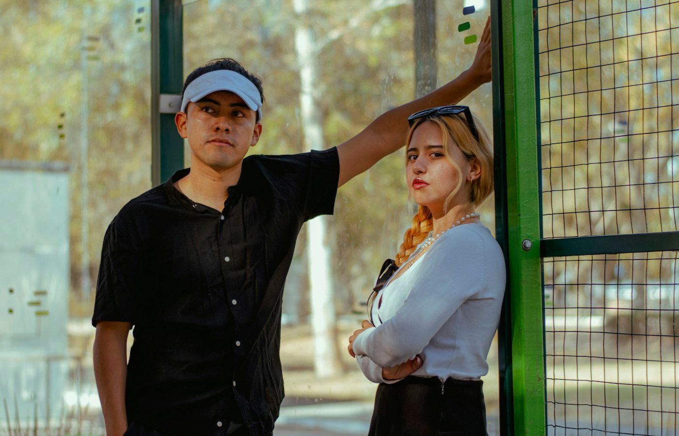 Un homme et une femme posent contre la vitre et le grillage d’un court de padel en extérieur